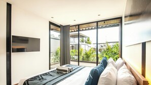 A modern bedroom with a large bed, a TV mounted on the wall, and a view of greenery outside. - Chic 4BR, 200m to Canggu's Blissful Beach Haven (Pererenan)