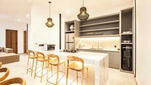 A modern kitchen with a central island, wooden bar stools, pendant lighting, and built-in shelving. - Chic 4BR, 200m to Canggu's Blissful Beach Haven (Pererenan)