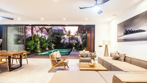 A modern living room with a pool view, a sofa set, a dining table, and a ceiling fan. - Chic 4BR, 200m to Canggu's Blissful Beach Haven (Pererenan)