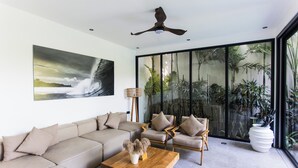 A modern living room with a large window, a ceiling fan, a sofa, armchairs, and a coffee table. - Beachside Bliss: New 5BR Villa Canggu (Pererenan)