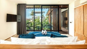 A modern hotel room with a large bed, a TV mounted on the wall, and a view of a building and greenery outside. - Beachside Bliss: New 5BR Villa Canggu (Pererenan)