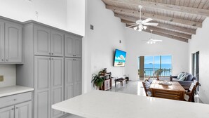 A spacious kitchen with white cabinets and a large island, a dining area with a view of the sea, and a ceiling fan. - Oceanfront Oasis: Dockside Bliss (Tavernier)
