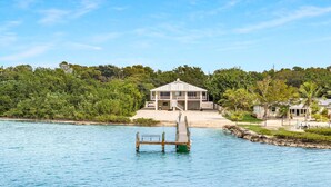 A beachfront property with a wooden dock extending into the water, a two-story building with a balcony, and lush greenery surrounding the area. - Oceanfront Oasis: Dockside Bliss (Tavernier)