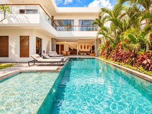 A modern pool area with lounge chairs, a clear pool, and tropical plants.