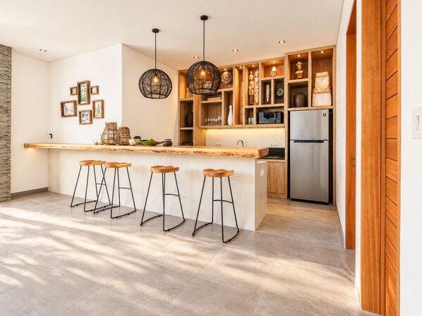 A modern kitchen with a central island, bar stools, pendant lighting, and a built-in refrigerator.
