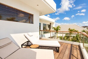 Un balcon moderne avec un fauteuil de salon blanc, une petite table et une terrasse en bois.