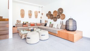 Een moderne woonkamer met een hoekbank, poufs, een glazen salontafel en decoratieve wandkunst.