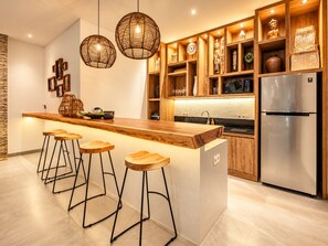 Eine moderne Küche mit einer Holzinsel, Barhocker, Pendelleuchten und eingebauten Regalen mit Dekorationselementen.