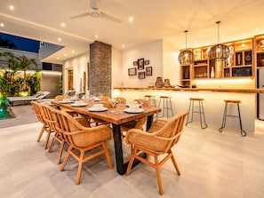 A modern dining area with a long wooden table, wicker chairs, and a bar with stools. - Coastal Comfort: Cozy 4BR Villa, 300m to Finns (Kecamatan Kuta Utara)