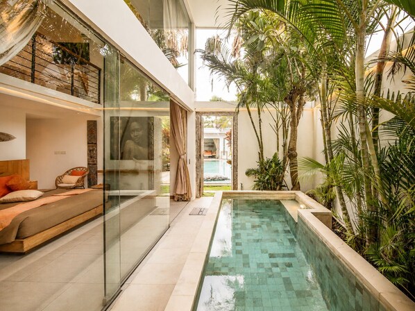 Un interior moderno con un dormitorio con paredes de cristal, piscina y plantas tropicales.