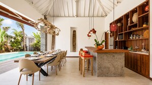 A modern kitchen with a bar area, a dining table set for six, and a poolside view. - Luxurious 5BR Dream Villa, 200m to Berawa Beach (Canggu)
