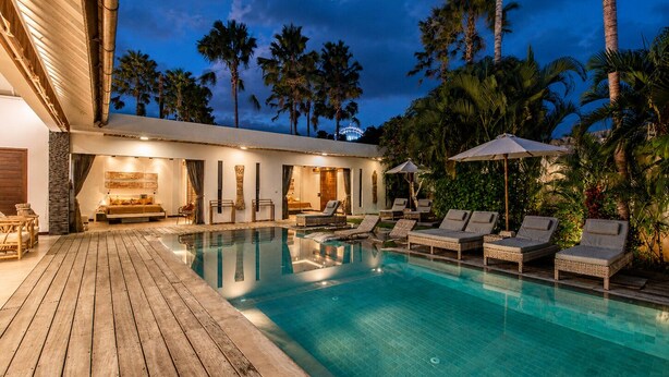 A poolside area with lounge chairs, a wooden deck, and a building with a modern design. - Luxurious 5BR Dream Villa, 200m to Berawa Beach (Canggu)