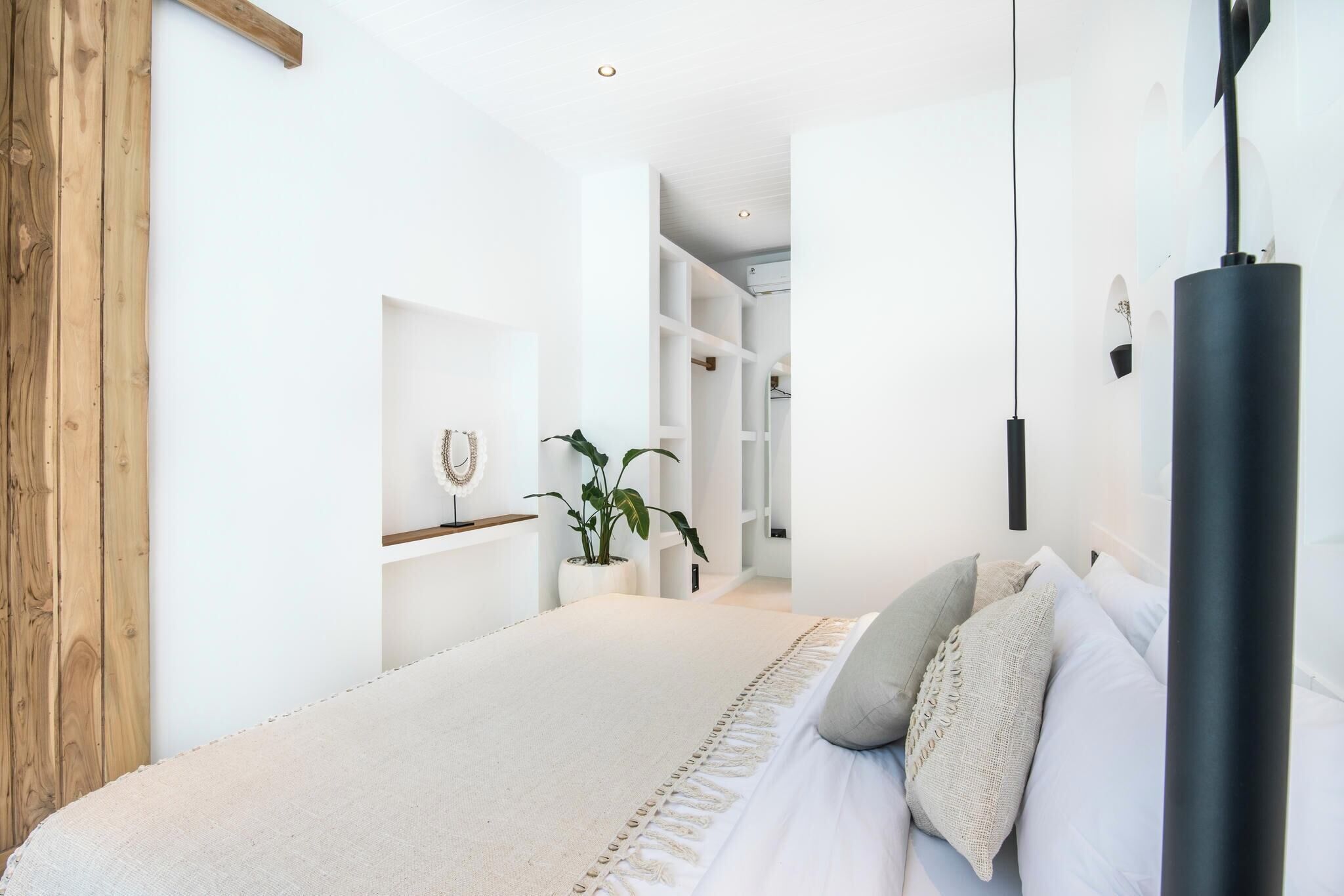 A bedroom with a large bed, a wooden door, a white wall, and a plant.