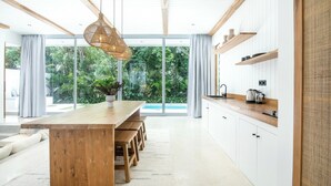 A modern kitchen with a wooden island, white cabinetry, and a large window overlooking greenery. - New 2br villa 4mins to Bingin beach (Uluwatu)