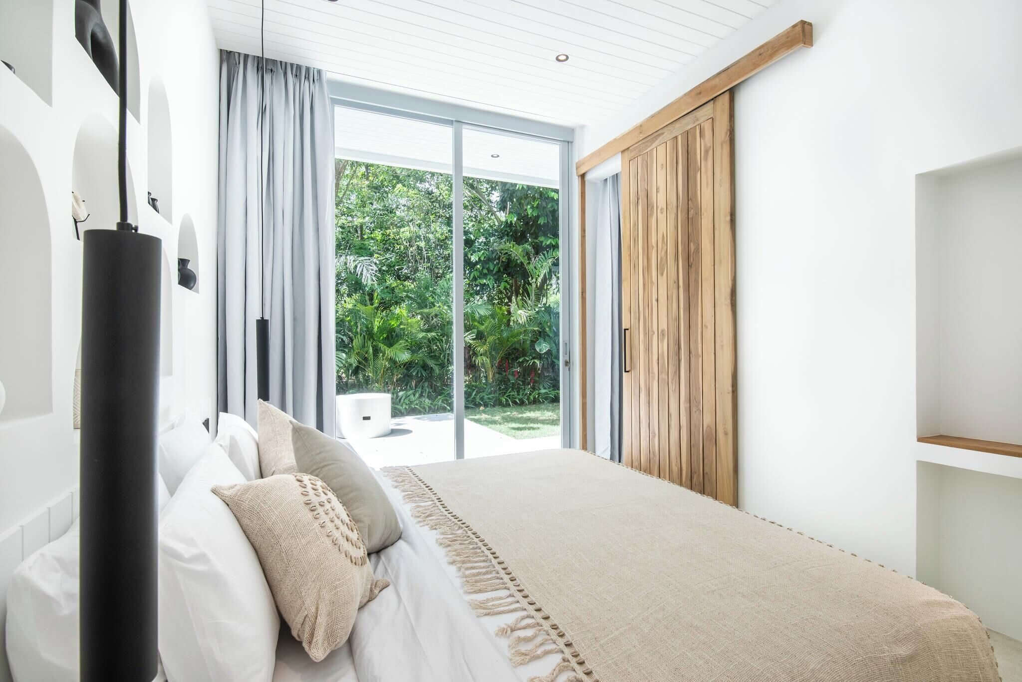 A bedroom with a large bed, a wooden wardrobe, and a sliding glass door leading to a garden.