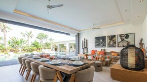 A modern dining area with a long wooden table set for six, surrounded by cushioned chairs. - Splendid 6BR Villa, Just 400m to the Shoreline (Kuta Utara)