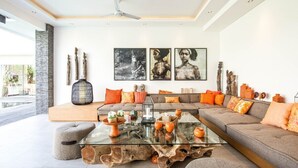 A modern living room with a glass coffee table, a grey sofa, and a large window. - Splendid 6BR Villa, Just 400m to the Shoreline (Kuta Utara)