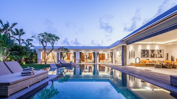 A modern house with a swimming pool, outdoor seating, and a well-lit interior. - Splendid 6BR Villa, Just 400m to the Shoreline (Kuta Utara)