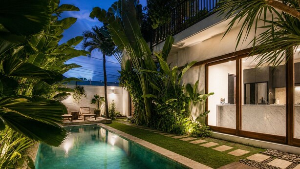 Un espace piscine extérieur moderne, doté d’une terrasse en bois, d’un coin salon avec une table et des chaises, et d’une pelouse bien entretenue.