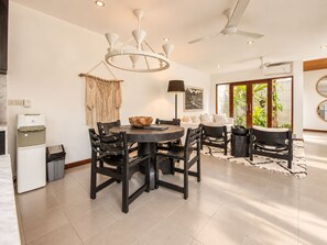 Un'elegante zona pranzo con tavolo rotondo, sedie nere, un lampadario e una ventola a soffitto.
