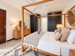 Un dormitorio moderno con cama con dosel, mesita de noche de madera, espejo redondo y una obra de arte grande colgada en la pared.
