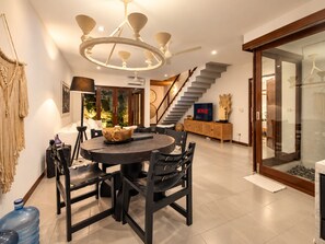 A modern living room with a round dining table, a staircase, and a large water dispenser. - Exquisite 2BR Villas, Brawah, 300m to Beach (Kuta Utara)
