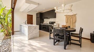 A modern kitchen with a marble island, dark cabinetry, and a dining area with a round table and chairs.
