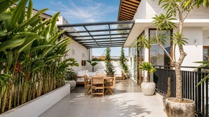 Une terrasse extérieure moderne, dotée d’un toit en verre, d’une table à manger et de divers pots de plantes.