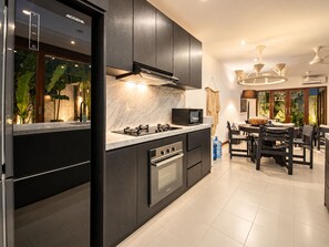 Une cuisine moderne avec des meubles de couleur sombre, une cuisinière à gaz, un four à micro-ondes et un coin repas comprenant une table et des chaises.