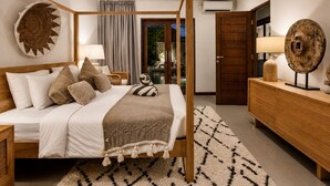 Un lit à baldaquin avec un cadre en bois, une table de chevet avec une lampe, un élément de décoration circulaire fixé au mur, et une vue sur une pièce dotée d’une porte en verre.