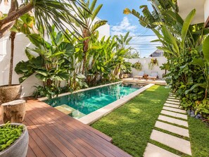 A swimming pool surrounded by lush greenery, a wooden deck, and a stone pathway. - Exquisite 2BR Villas, Brawah, 300m to Beach (Kuta Utara)