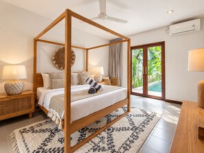 A four-poster bed with a wooden frame, a woven rattan nightstand, a patterned rug, and a view of a swimming pool through a glass door. - Exquisite 2BR Villas, Brawah, 300m to Beach (Kuta Utara)