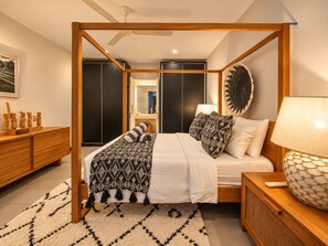 Una camera da letto con un letto a baldacchino, un comodino con una lampada, un tavolino in legno, una coperta decorativa e un elemento decorativo a parete.