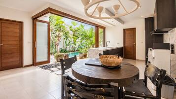 A modern kitchen with a built-in oven, a dining area with a round table and chairs, and a view of a lush garden through large windows.