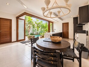 A modern kitchen with a built-in oven, a dining area with a round table and chairs, and a view of a lush garden through large windows. - Exquisite 2BR Villas, Brawah, 300m to Beach (Kuta Utara)