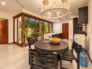 A modern kitchen with a round dining table, a built-in stove, and a large window overlooking a garden. - Exquisite 2BR Villas, Brawah, 300m to Beach (Kuta Utara)