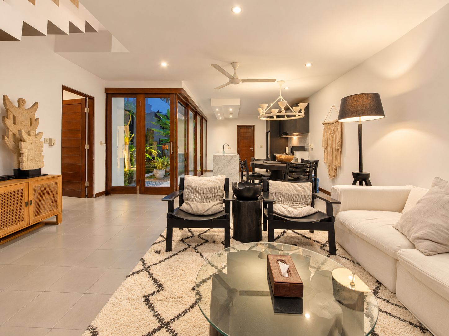 A modern living room with a glass coffee table, a sofa, and a dining area with a chandelier.