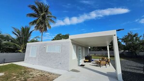 A modern outdoor patio area with a covered seating space and a small building with windows. - Spacious Home with Beach Gear and Outdoor Space (Vieques)