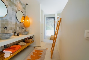 Een moderne badkamer met een witte wastafel, twee spiegels en een houten plank met toiletartikelen.