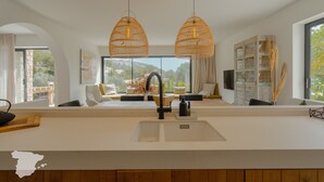 Una cocina moderna con un amplio ventanal, dos lámparas colgantes y una estantería empotrada.