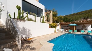 Un área de piscina moderna con borde curvo, mobiliario exterior y cactus en la fachada del edificio.