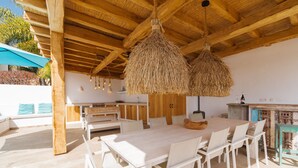 Un amplio espacio de comedor al aire libre con una gran mesa y sillas, un colgante de techo de paja y una estructura de techo de madera.