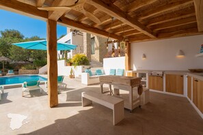 Een terras buiten met een zwembad, zitplaatsen en een houten pergola.