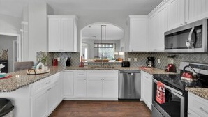 Une cuisine avec des meubles blancs, des plans de travail en granit, un lave-vaisselle, une cuisinière et un four à micro-ondes.