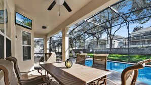 Un patio couvert avec une piscine, du mobilier d’extérieur et un écran de télévision.