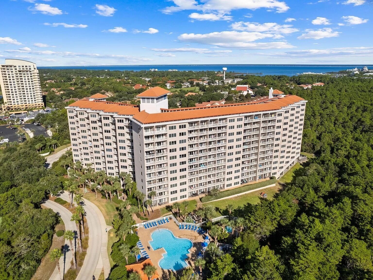 A high-rise hotel with multiple balconies, a swimming pool, and a view of the ocean.