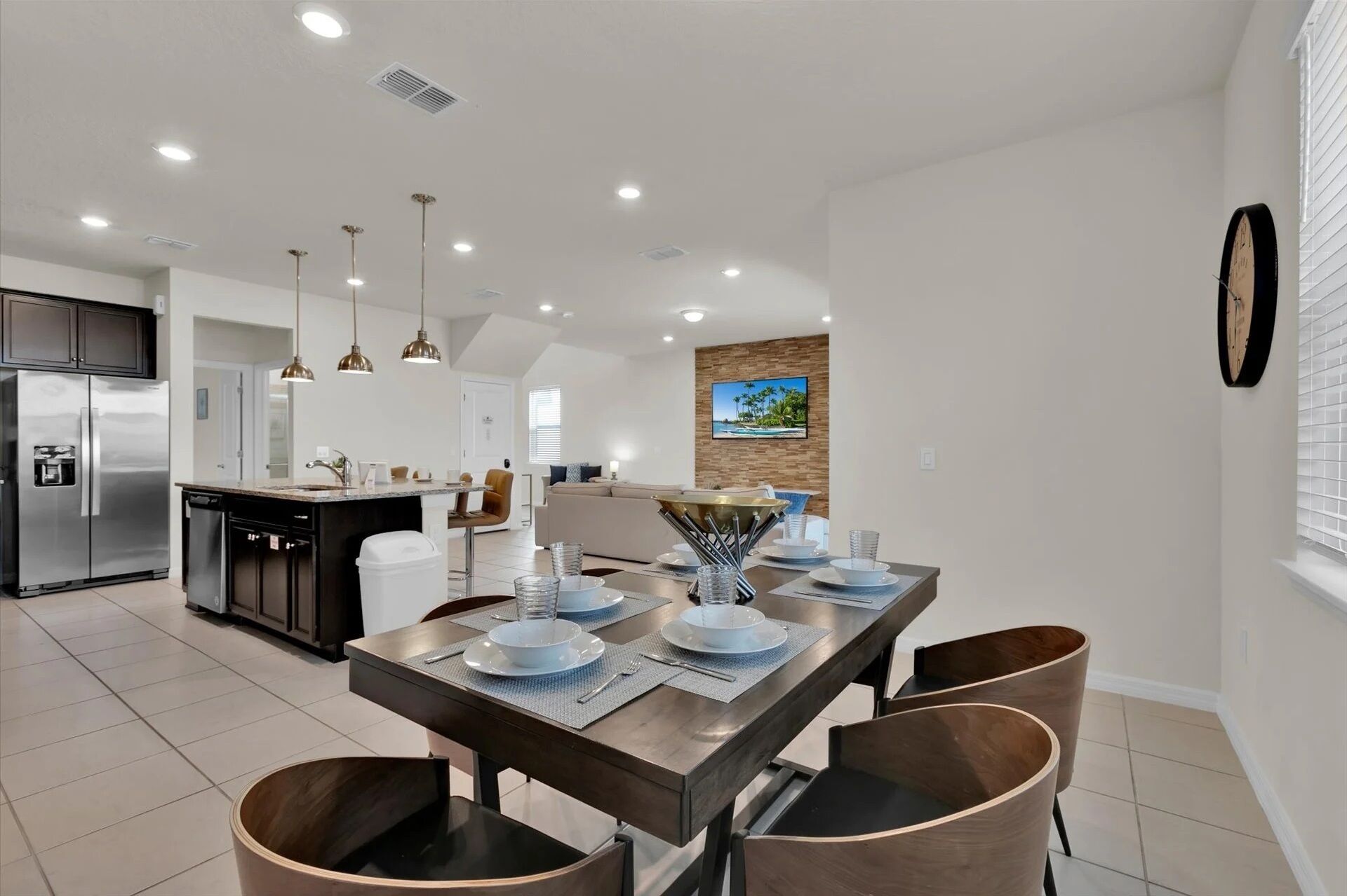 A modern kitchen with a central island, stainless steel appliances, pendant lighting, and a dining area with a wooden table and chairs.