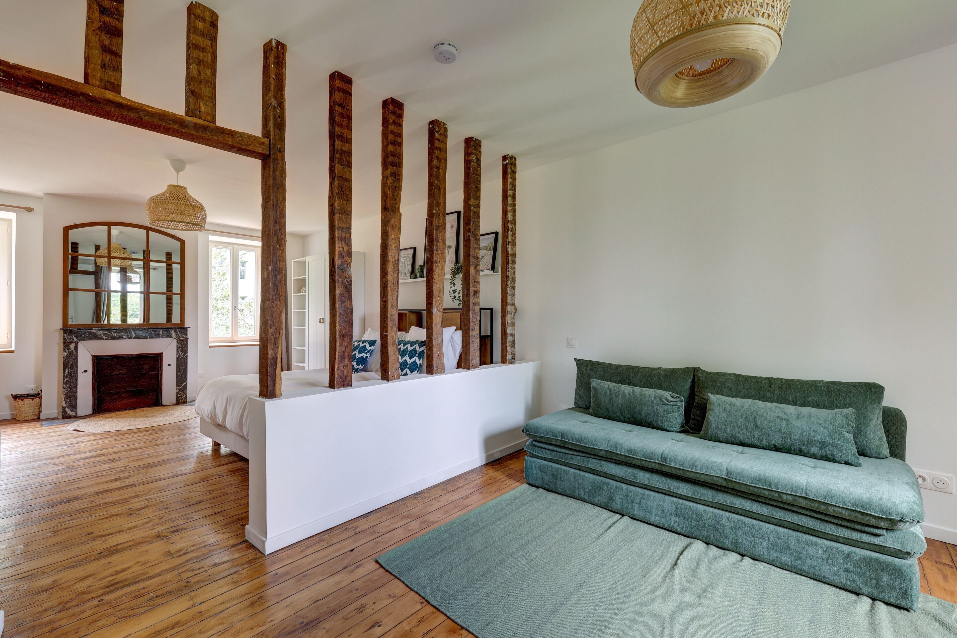 A room with a wooden floor, a green sofa, a white console table, and a fireplace.