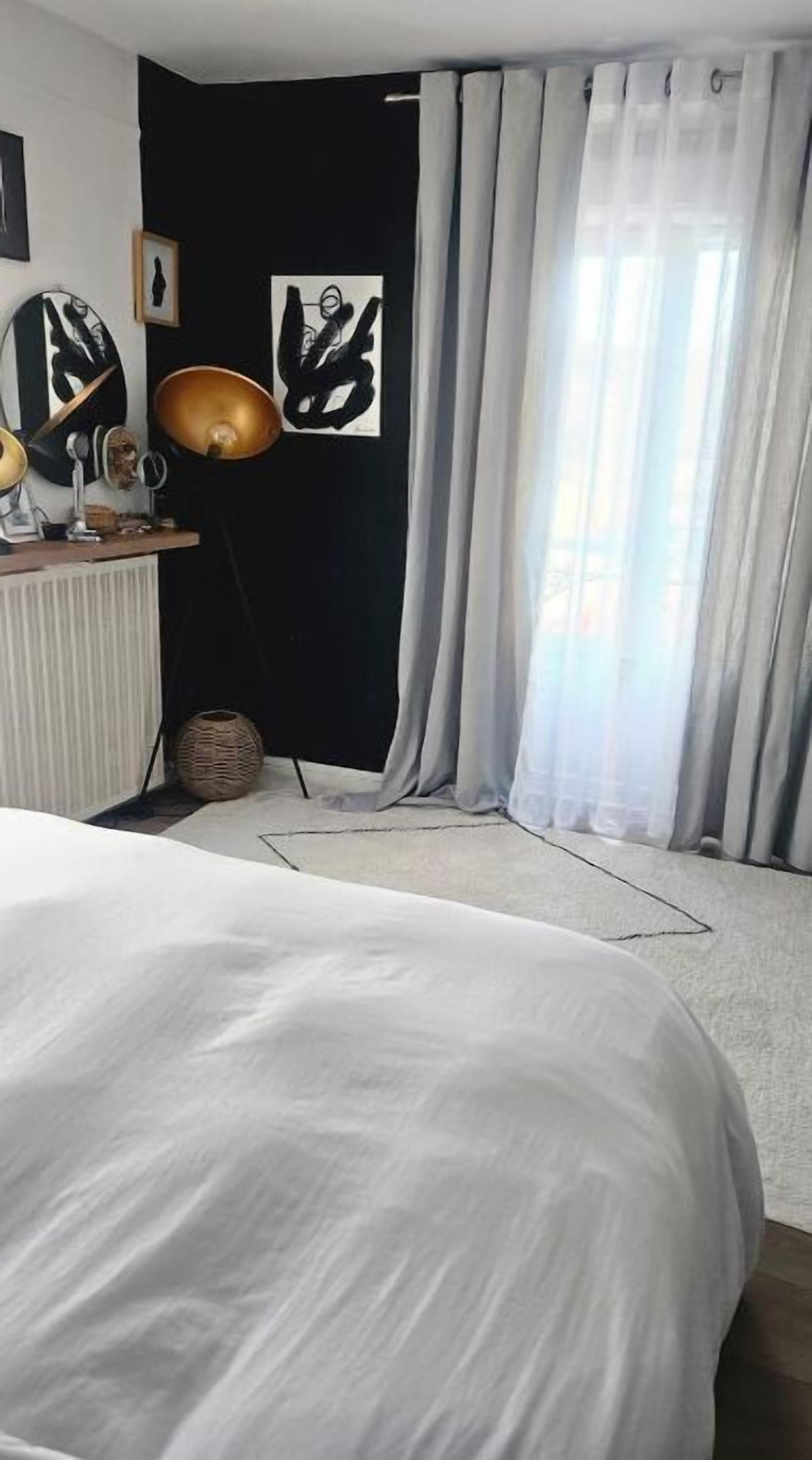 Une chambre à coucher avec un lit, une commode, une lampe et une fenêtre avec des rideaux.