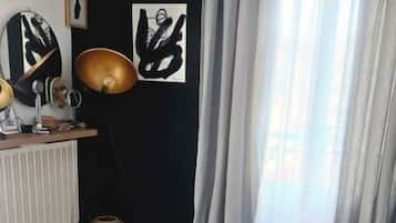 Une chambre à coucher avec un lit, une commode, une lampe et une fenêtre avec des rideaux.